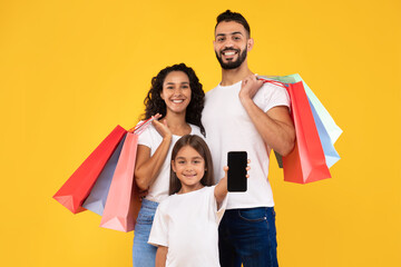 Middle-Eastern Family Showing Smartphone Posing With Shopping Bags, Yellow Background