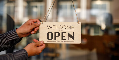 Close up of  Store owner turning open sign broad through the door glass and ready to serve. hotel service, cafe-restaurant, retail store, small business owner concept 