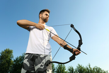Man with bow and arrow practicing archery outdoors, low angle view