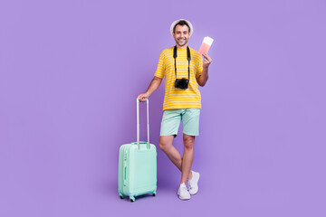 Full body photo of young man happy positive smile tourism holiday suitcase camera passport isolated over violet color background