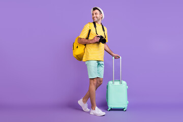 Full body photo of brunet happy positive man walk hold luggage camera casual clothes hat isolated on violet color background