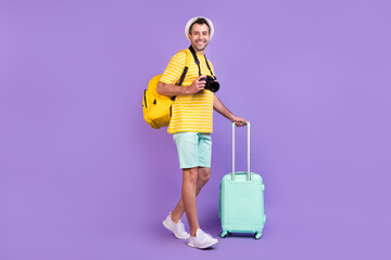 Full length profile side photo of young man happy positive smile go walk baggage camera trip isolated over violet color background