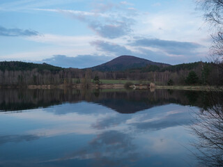 Evening view on blue calm forest lake, fish pond Kunraticky rybnik with birch and spruce trees growing along the shore, blue sky and clouds reflecting on water. Nature background, spring landscape.