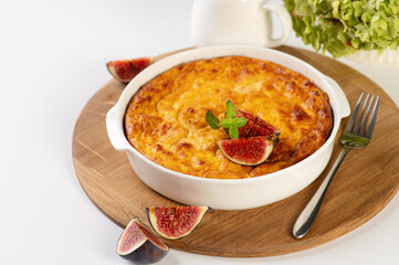 curd casserole with pumpkin in a round white shape on a wooden board, a white table decorated with figs, restaurant serving