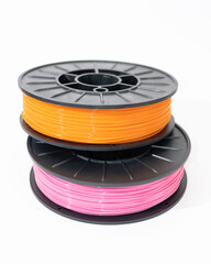 PLA plastic for 3D printing. From renewable resources such as cornstarch or sugarcane. Environmentally friendly plastic in spools, yellow and pink colors on a white background