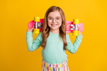 Photo of young preteen girl happy positive smile hold skateboard on shoulders isolated over yellow...