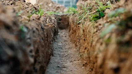 Fotobehang Dig a trench. Earthworks, digging trench. Long earthen trench dug to lay pipe or optical fiber. Construction the sewage and drainage. View from the trench. Clay soil. Part of the image is blurred © MIKHAIL