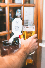 Man's hand holding glass of beer at bar, celebrating, sitting at table