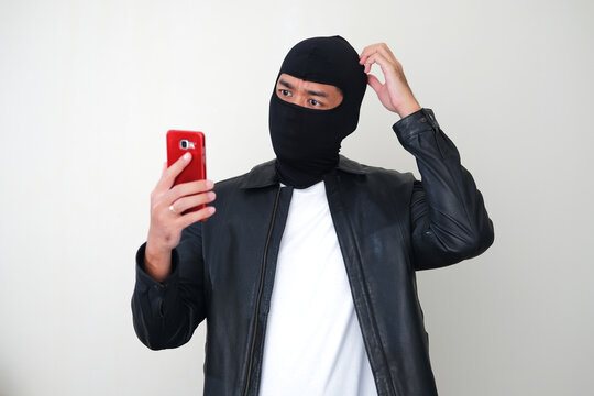 Bad guy wearing balaclava showing confused gesture while looking to mobile phone
