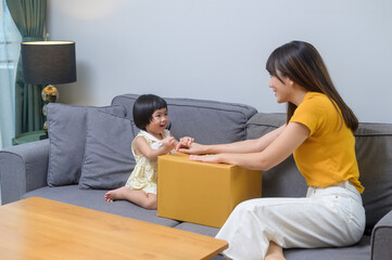 Happy mom with daughter opening cardboard box in living room at home