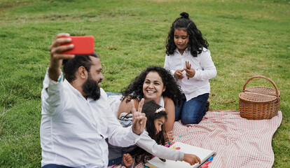 Happy indian family enjoy day outdoor at park with picnic and toys while taking a selfie using...