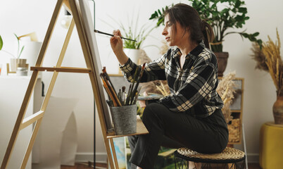 A young woman artist paints in her apartment with oil paints. Female student draws in art studio.Fine art study concept.