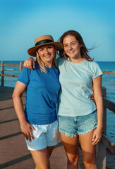 Happy mother and teenage daughter standing on pier at sea coast, embracing and smiling