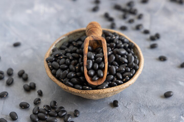 Bowl full of dry black beans with a scoop on grey table close up