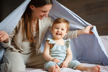 Mom plays with her little daughter in the bedroom. Gentle hugs and fun.