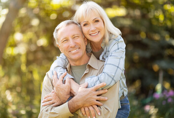 Happy elderly man and woman spending time together, embracing, resting in garden at sunny autumn day
