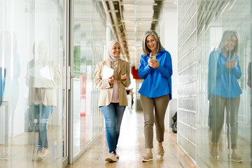 Multiracial two women smiling and talking while walking in office