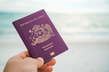 a hand holding a red passport on a beach