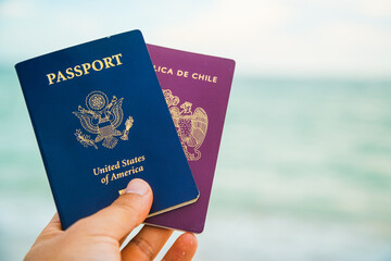 a hand holding two passport a red and a blue one on a beach