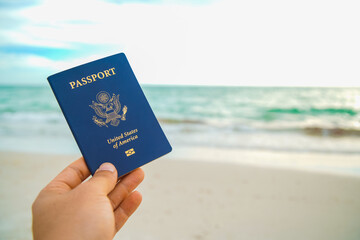 a hand holding a blue passport on a beach