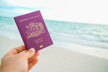 a hand holding a red passport on a beach