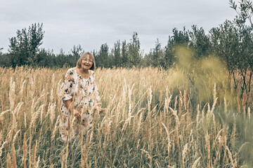 An elderly woman in the tall grass with spikelets. Autumn