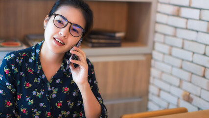 Asian businesswoman wearing glasses and using mobile phone to contact work, online merchandising concept, work from home concept.