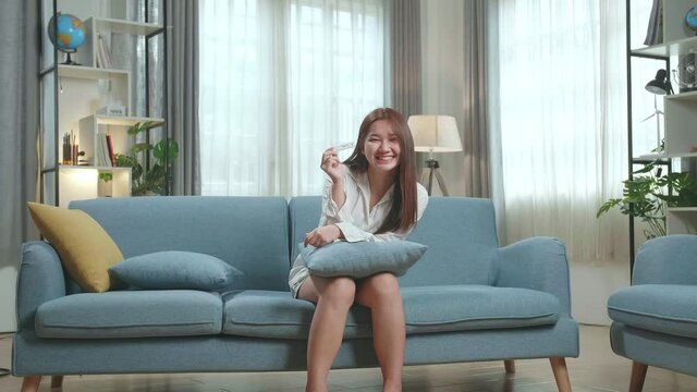 Happy Young Asian Woman Holding Pregnancy Test And Warmly Smiles To Camera In The Living Room At Home
