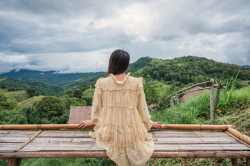 Asian woman in yellow dress sitting at wooden terrace among the mountain on vacation