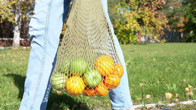 Woman walks with a braided string bag of fresh fruit. Life without plastic waste. Low-waste lifestyle. Sustainable ecological lifestyle