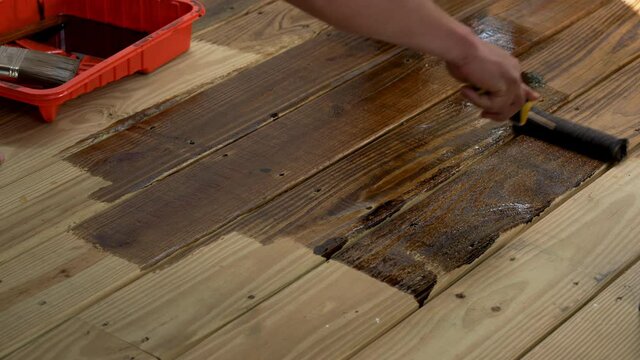 A person stains a pressure-treated deck with a paint brush.