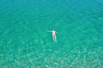 Young woman in a bikini swimming in sea water on the beach. View from above. Top, drone view