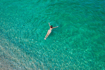Young woman in a bikini swimming in sea water on the beach. View from above. Top, drone view