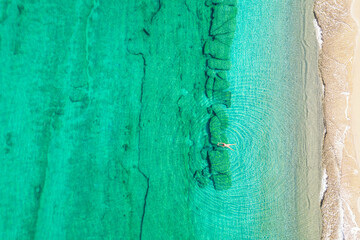 Relaxing aerial beach view with calm sea water and stone, slabs, lump, coral. Summer vacation. Blue ocean lagoon, sea shore, coastline. Drone, copter top view.