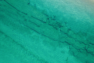 Relaxing aerial beach view with calm sea water and stone, slabs, lump, coral. Summer vacation. Blue ocean lagoon, sea shore, coastline. Drone, copter top view.