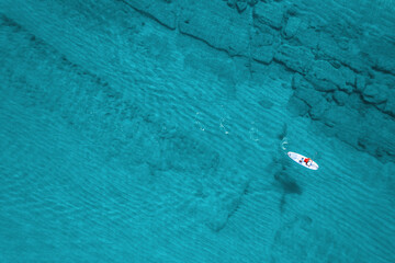 Alone man rowing on SUP board on aquamarine, blue sea water with coral in lagoon. Aerial top view paddleboard. Surfing