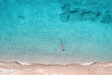 Young woman in a swimsuit swimming in sea water on the beach. View from above. Top, drone view
