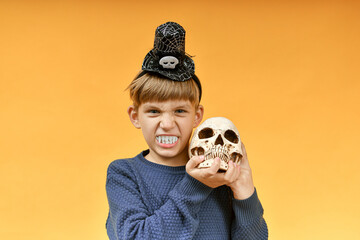 Angry boy with vampire teeth holds a skull in his hands. Halloween image.