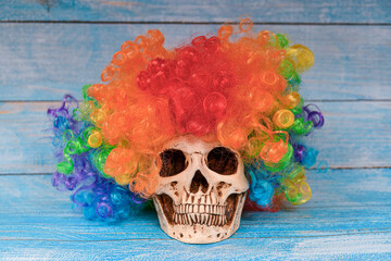 Skull with golden crown and clown wig on a blue wooden background.