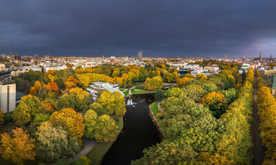 Park in Riga with trees in autumn colors. Colorful sunset over the city panorama. Downtown in...
