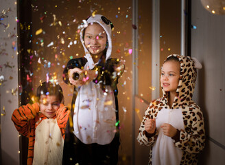 Obraz na płótnie Canvas Three children in funny rompers releasing Christmas cracker at home party