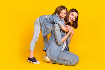 Photo of two relaxed fooling sisters wear jeans shirts smiling sitting floor embracing isolated yellow color background