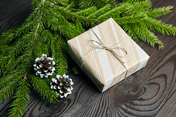 Gift box with green Christmas tree branch and cones on wooden background