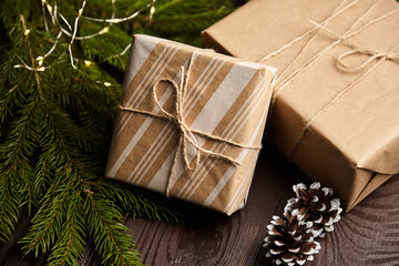 Gift boxes with Christmas light and tree branch with cones on brown wooden