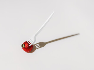 Plastic fork stuck in a red tree ball ornament on a white background. Creative New Year and Merry Christmas concept. Minimal festive dinner backdrop. Fashion seasonal visual trend.