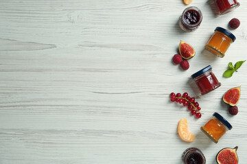 Jars of different jams and fresh ingredients on white wooden table, flat lay. Space for text