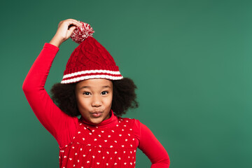 African american kid holding hat and pouting lips isolated on green