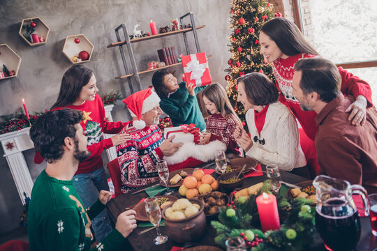 Photo portrait santa claus giving xmas presents to little kids sitting at table with full family in decorated apartment