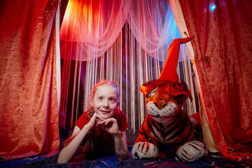 Young teenager girl during a stylized theatrical circus photo shoot in a beautiful red location....