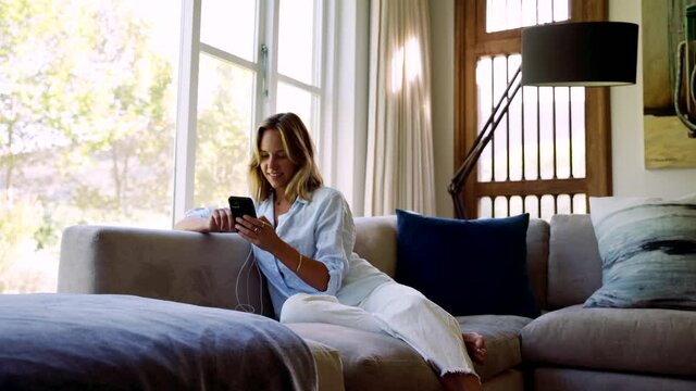 Caucasian female relaxing on couch typing on cellular device 